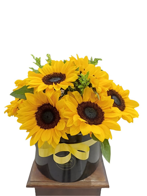 An arrangement of yellow roses with brown centers, arranged in a clear round vase.