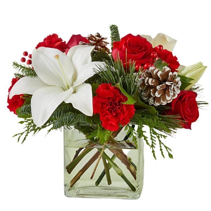 Arreglo navideño moderno con lirios blancos, rosas rojas y piñas en base de vidrio.