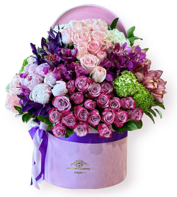 A floral arrangement featuring peonies, roses, hydrangeas, and orchids in shades of green, pink, and purple, presented in a purple container with a pink lid.