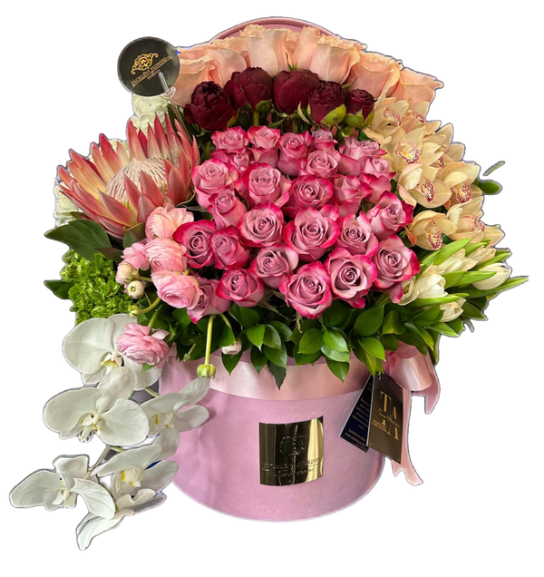 A floral arrangement featuring a mix of pink and red roses, white tulips, orchids, and green hydrangeas in a pink container.