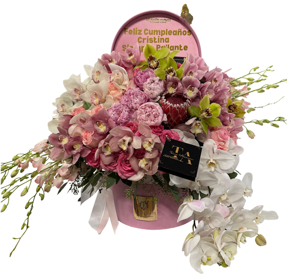 A floral arrangement featuring a variety of orchids in shades of pink, white, and green, presented in a box with a clear window and a greeting message.