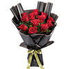 A dozen red roses arranged in a bouquet with black wrapping paper and a gold ribbon.