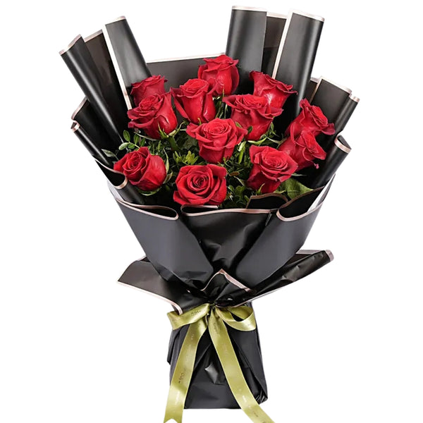 A dozen red roses arranged in a bouquet with black wrapping paper and a gold ribbon.