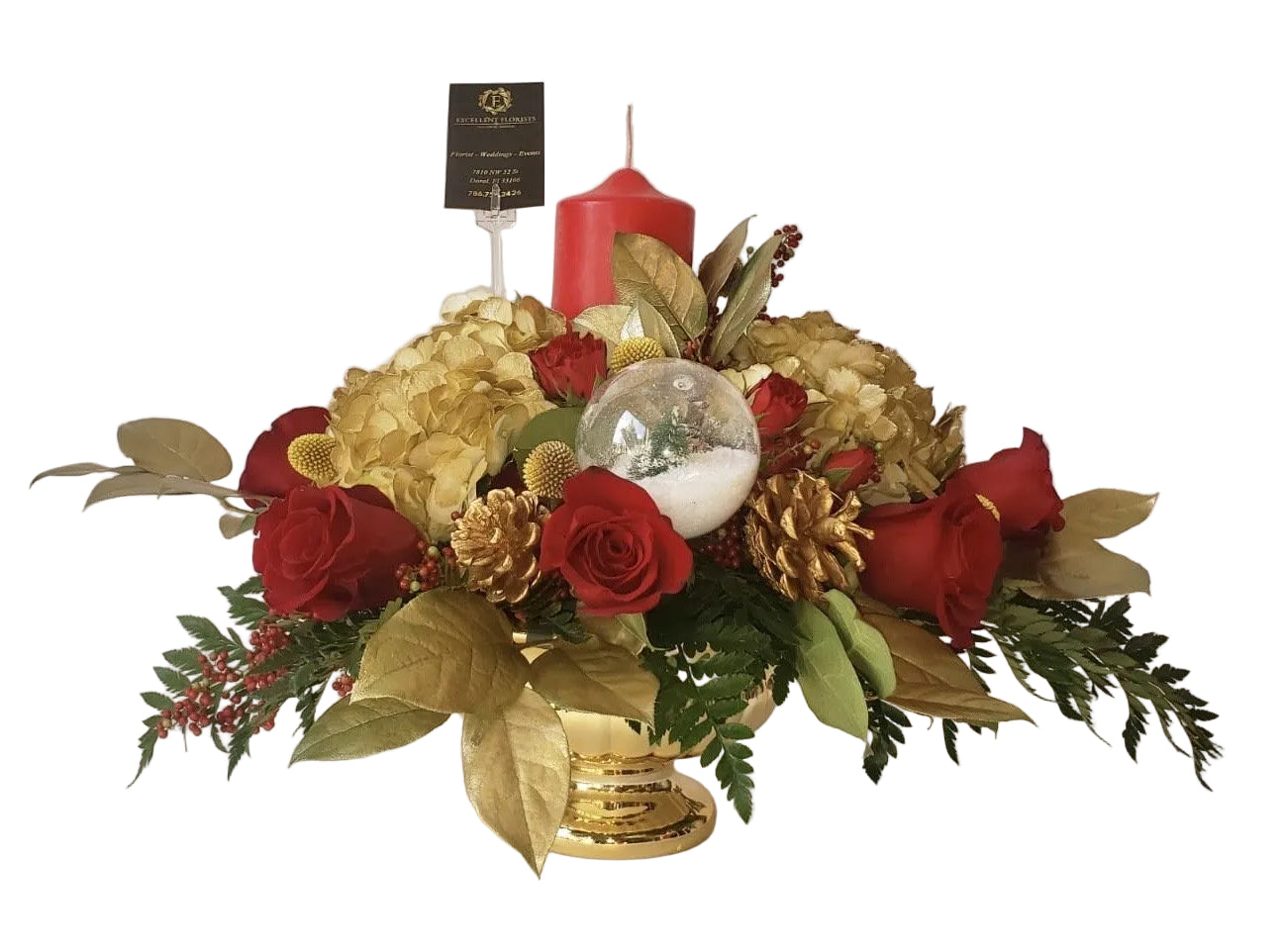 A floral centerpiece featuring roses, hydrangeas, pinecones, and berries with a red candle and a decorative glass ornament, all in a golden color palette.