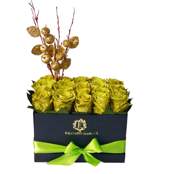 A box of preserved yellow and green roses, with decorative gold ornaments, presented in a black box with a green ribbon.