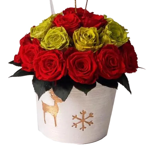A preserved rose bouquet with red, green, and yellow roses in a white pottery vase decorated with a golden deer design.