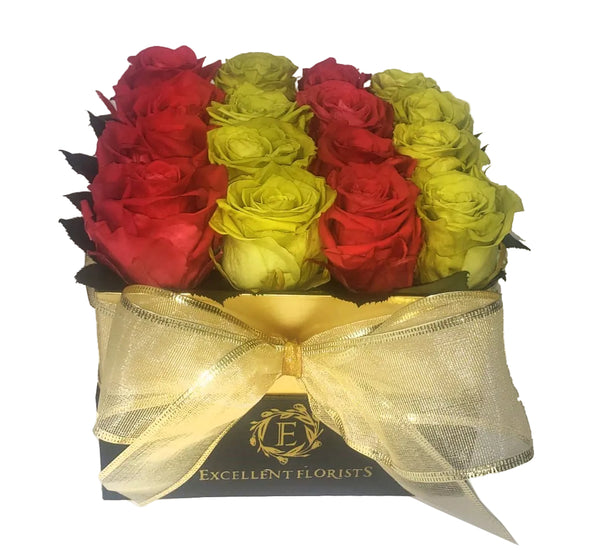 A medium square box of preserved roses with a mix of red, yellow, green, and pink colors, tied with a gold ribbon
