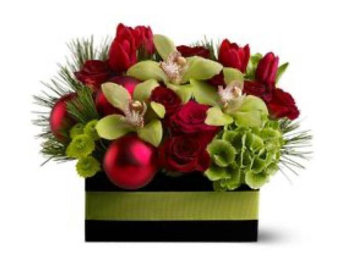 A floral arrangement featuring red roses, green orchids, and decorative greenery in a black box with a Christmas tree decoration.