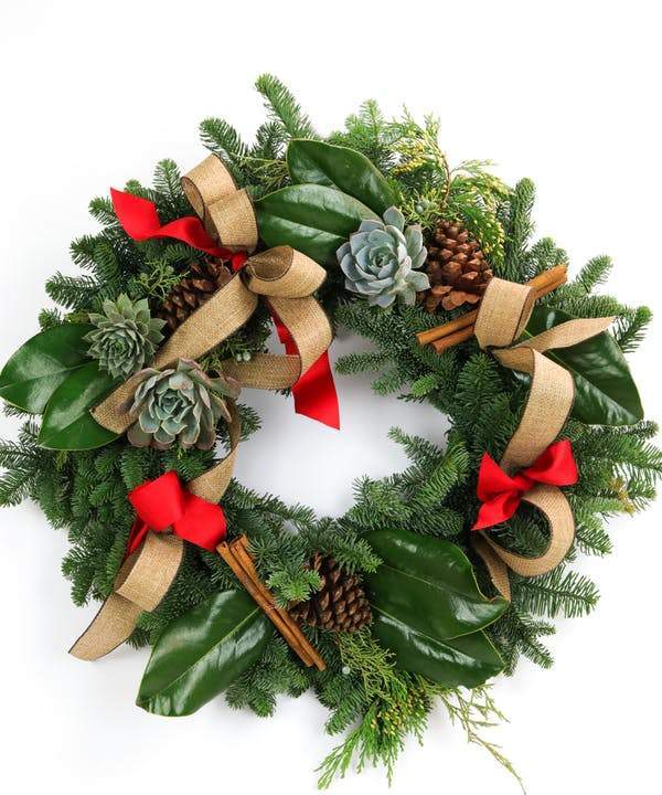 A round evergreen wreath decorated with red and burlap ribbon, greenery, pine cones, and magnolia leafs.